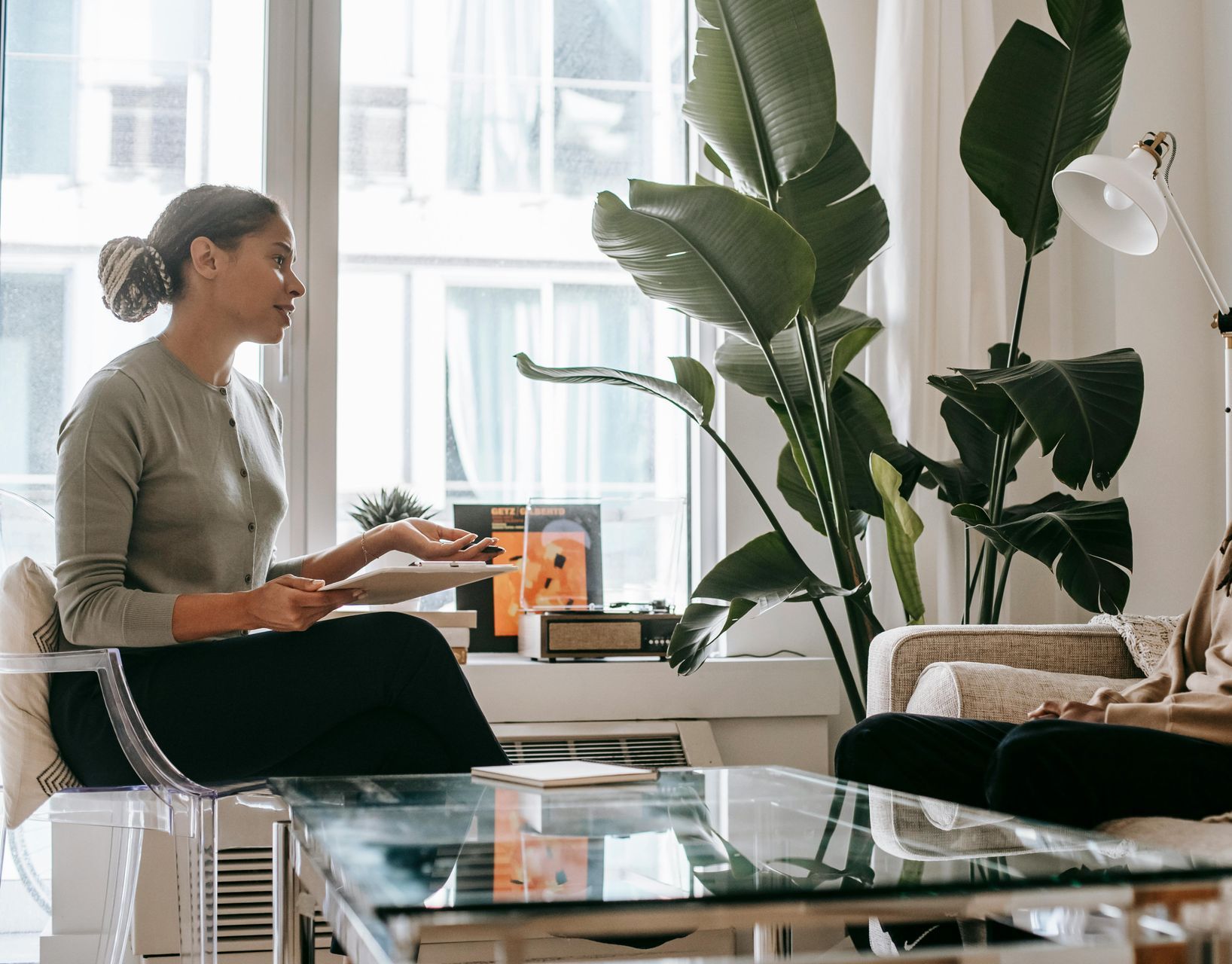Person sitting on a sofa in a bright living room with a glass coffee table and tall plants