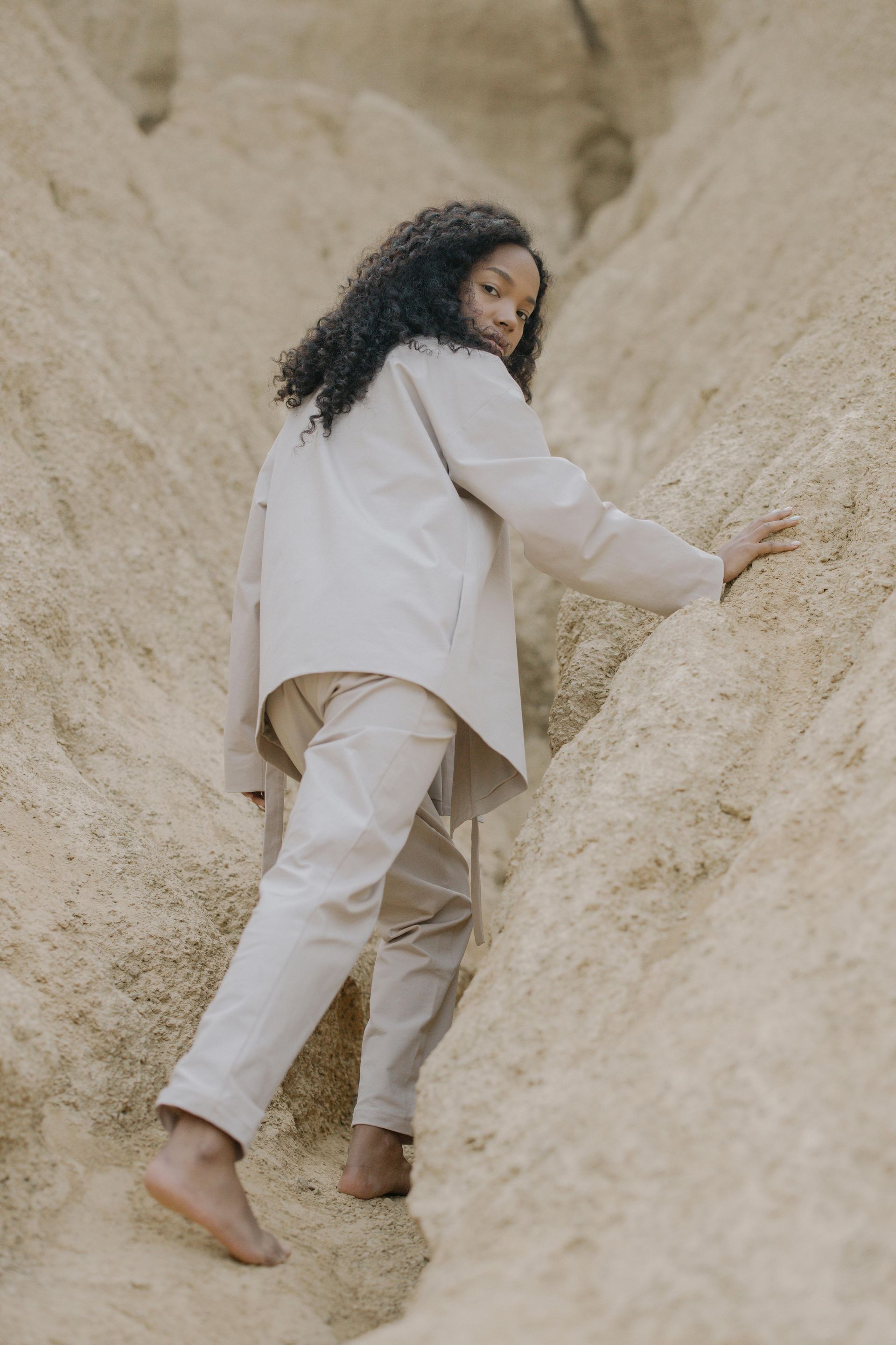 Person climbing a sandy rock slope in light-colored clothes