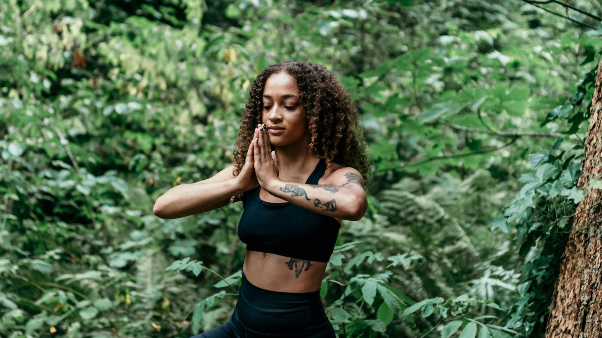 Woman in a black top posing outdoors in a lush green forest.
