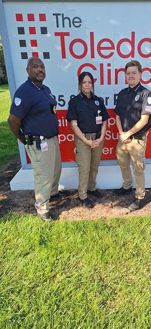 Three uniformed people stand in front of The Toledo Clinic sign.