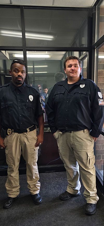 Two security guards in uniform stand indoors, facing forward.