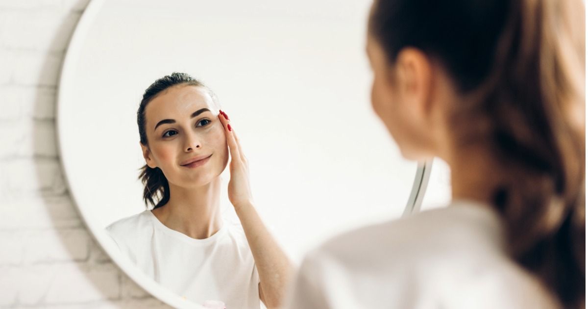 Woman smiling at her reflection in a round mirror while applying skincare