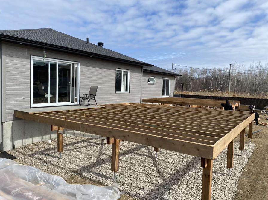 une grande terrasse en bois est en cours de construction devant une maison.