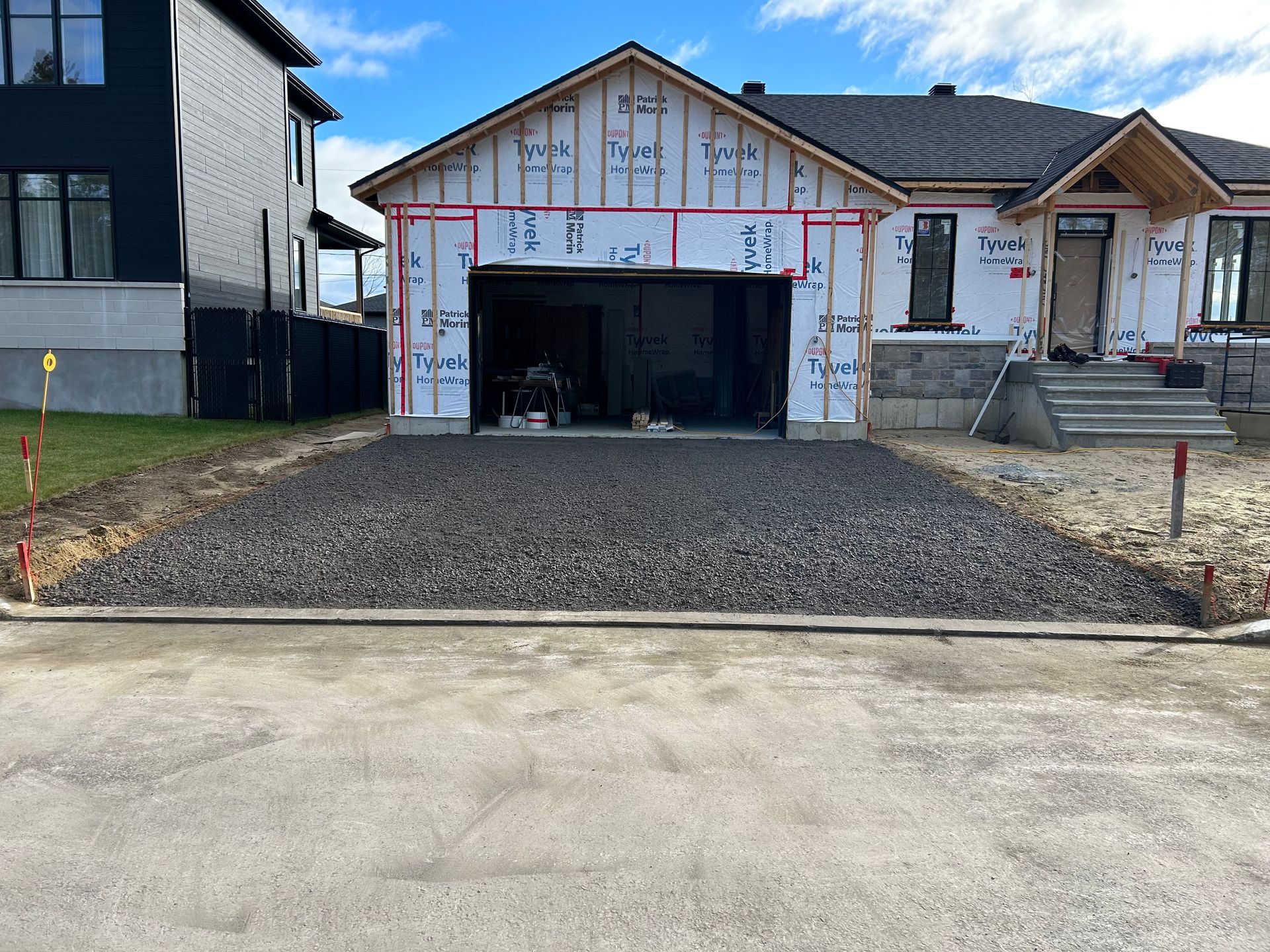 Une maison en construction avec une allée en gravier et un garage partiellement ouvert.