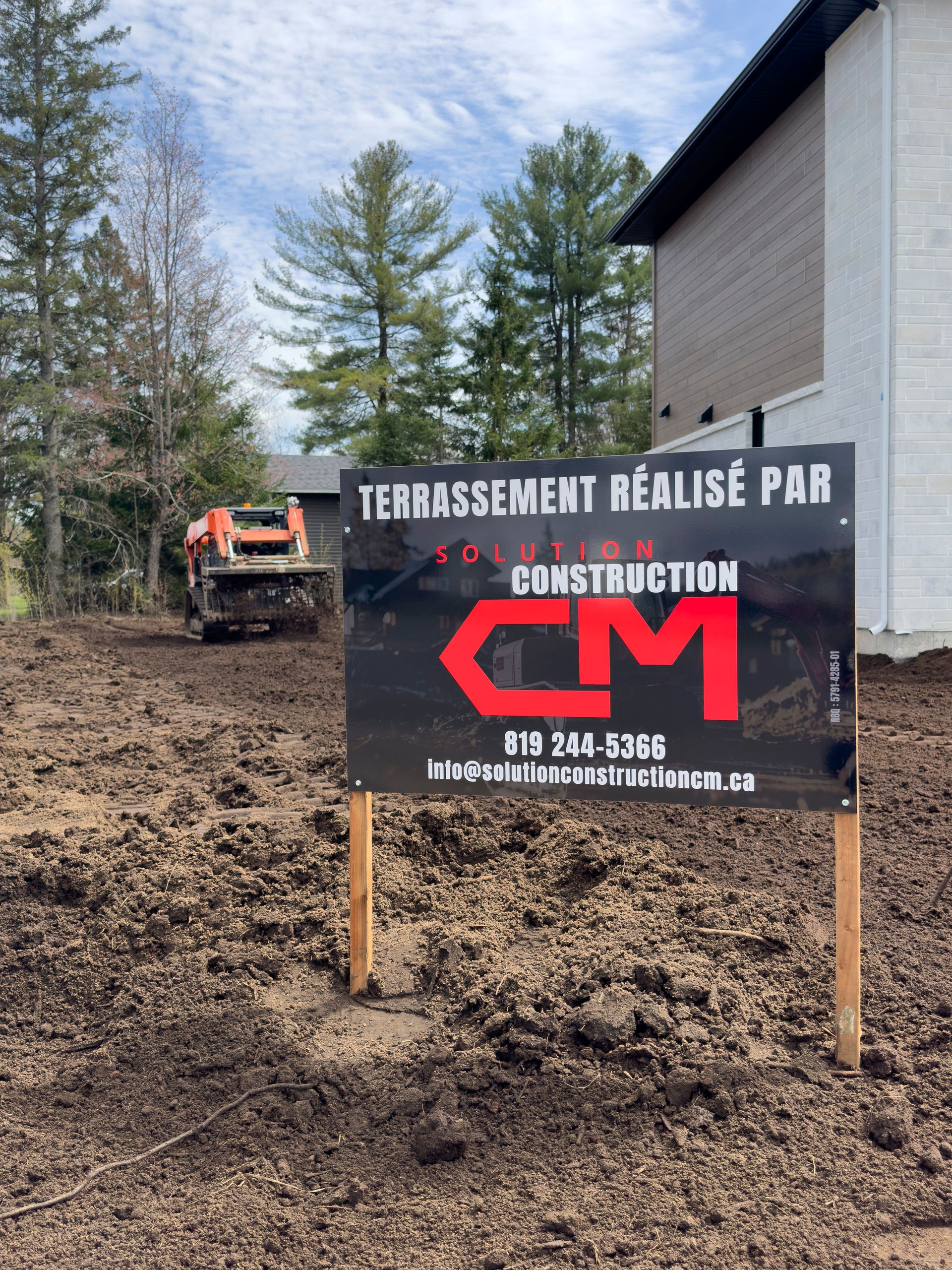Panneau « CM Construction » sur un chantier. Une petite pelleteuse est visible en arrière-plan.