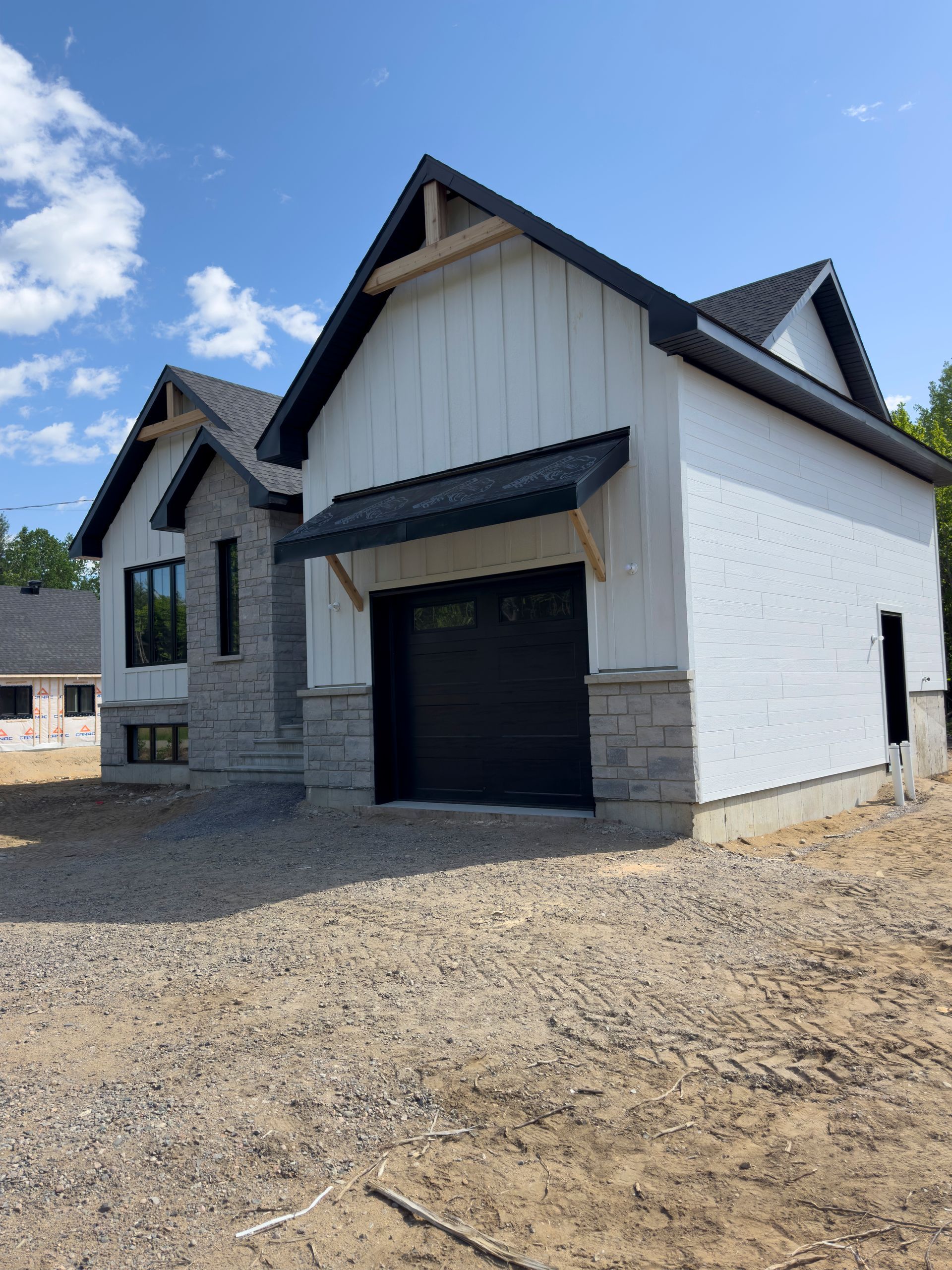 Une maison blanche avec une porte de garage noire et un toit noir