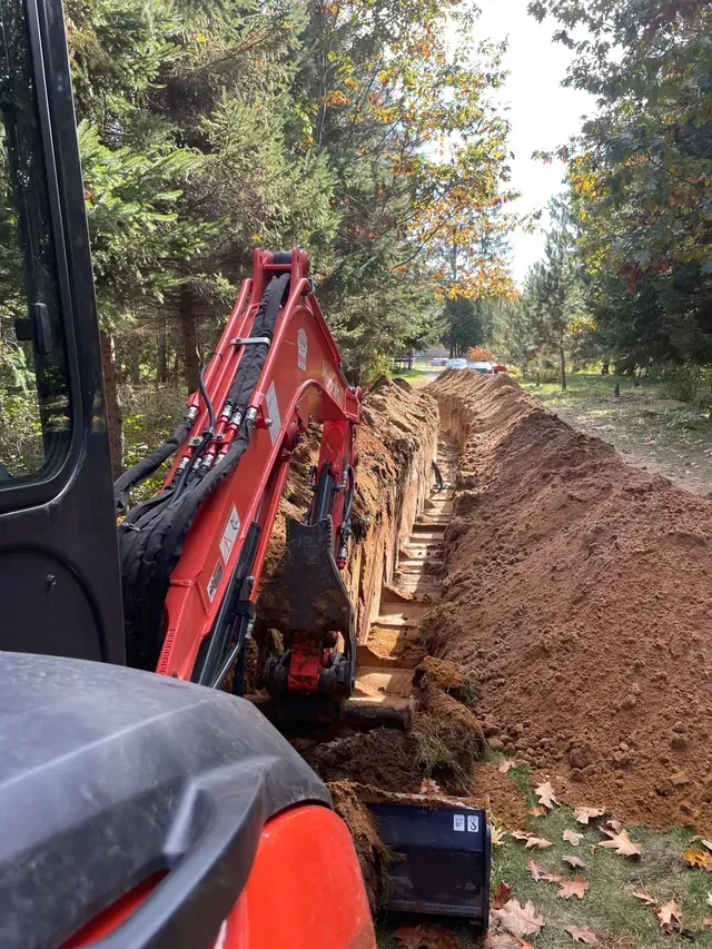 Une excavatrice rouge et noire creuse un trou dans le sol.
