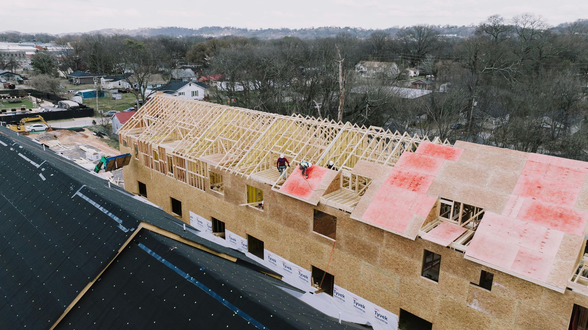 Vue en plongée de travailleurs du bâtiment installant un revêtement de toiture en contreplaqué sur la charpente en bois d'un bâtiment.