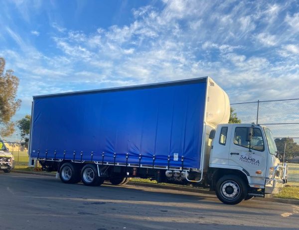 A white truck with a blue tarp is parked on the side of the road.