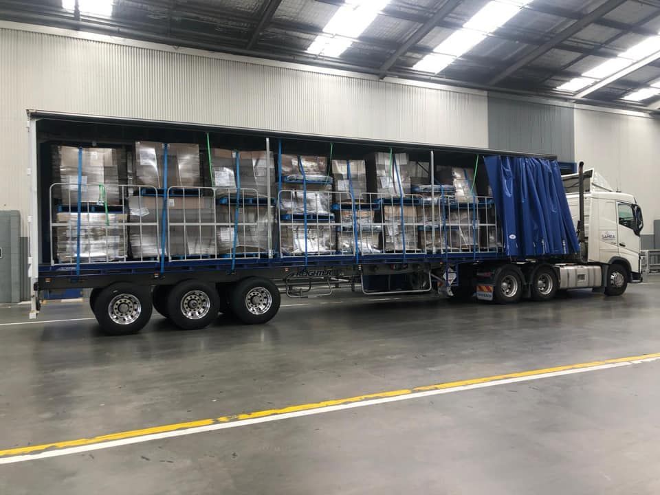 A semi truck is parked in a warehouse filled with lots of boxes.