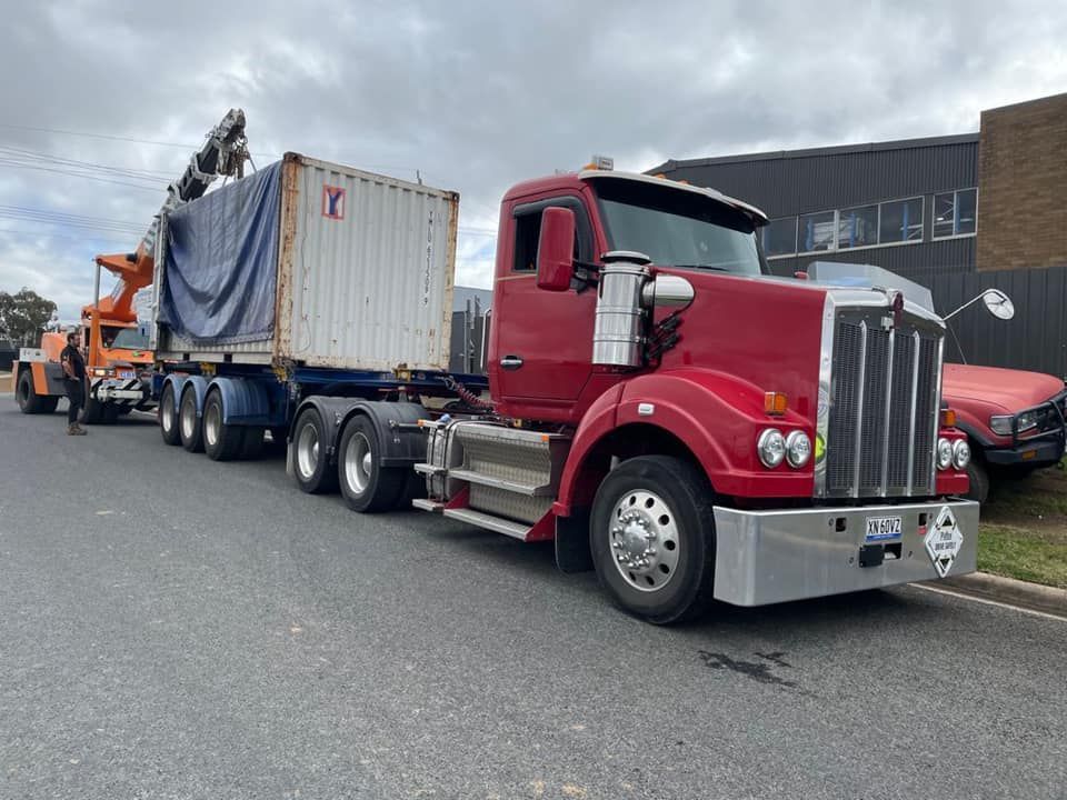A red semi truck is carrying a container down a street.