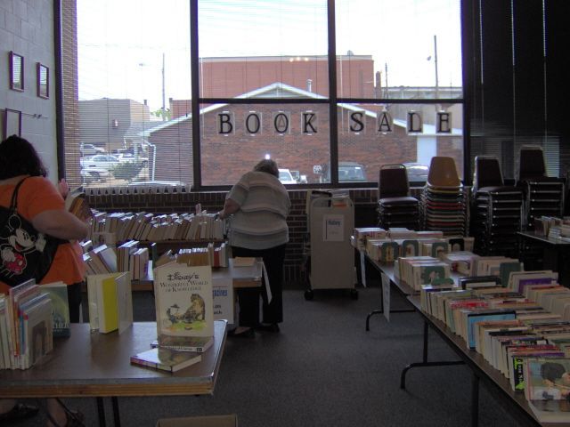 Book sale inside a building with a large window. People browse books on tables. 