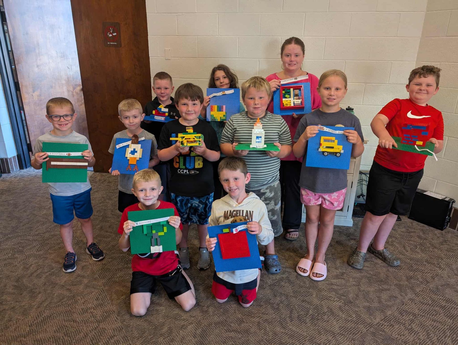 Children holding LEGO creations, posing indoors.