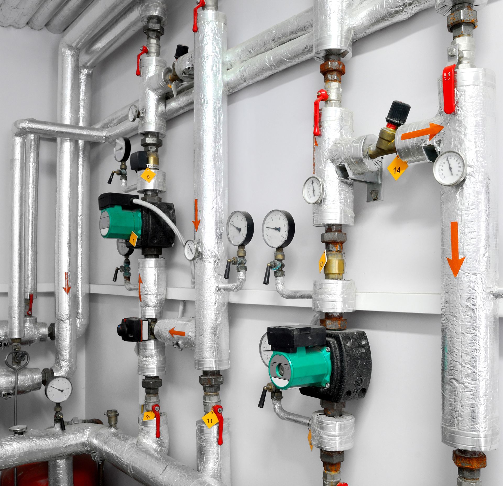 Insulated industrial pipes with valves, gauges, and pumps on a white wall