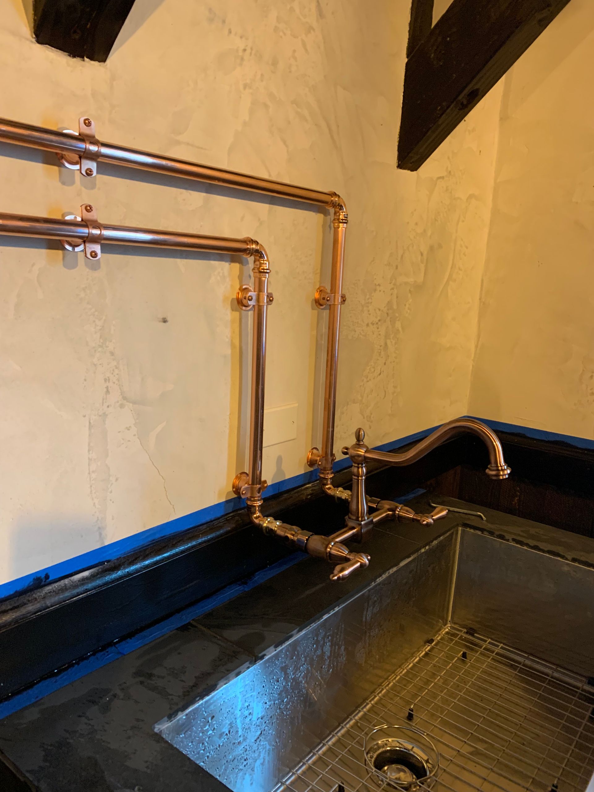 Copper pipes above a black utility sink in a corner with beige walls and blue trim