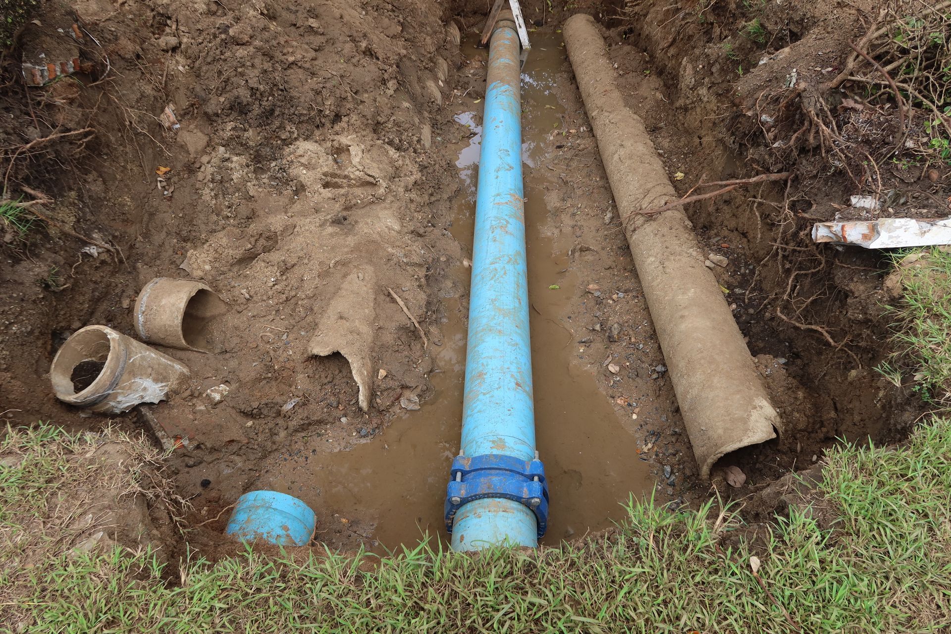 Blue water pipe in a dirt trench beside a broken pipe and soil, showing underground plumbing work