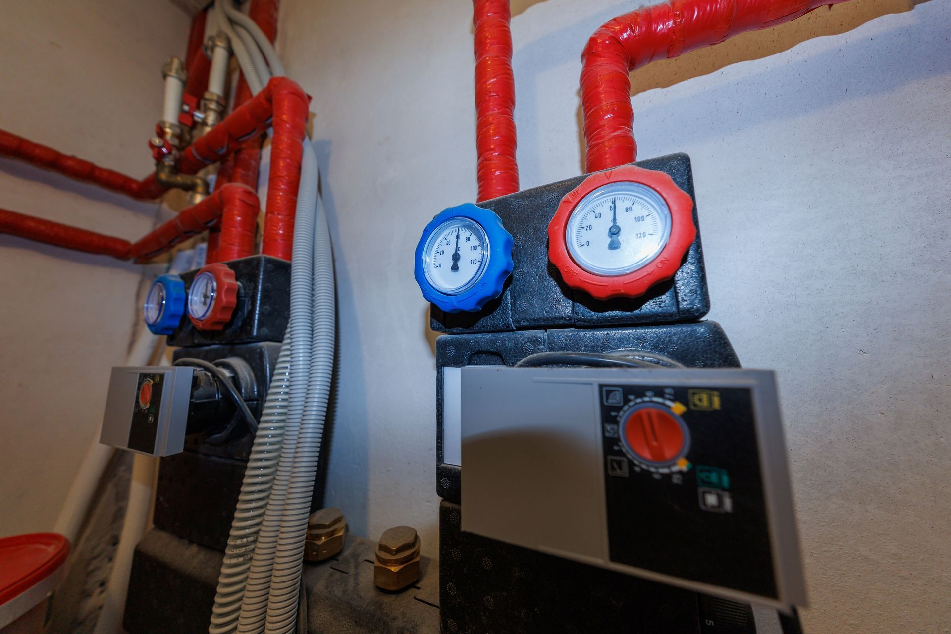 Red heating pipes with blue and red gauges above a boiler in a utility room