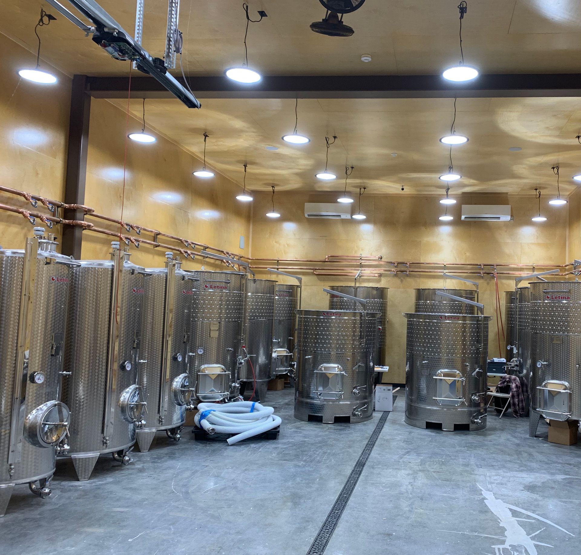 Wine cellar with rows of stainless steel fermentation tanks under bright ceiling lights