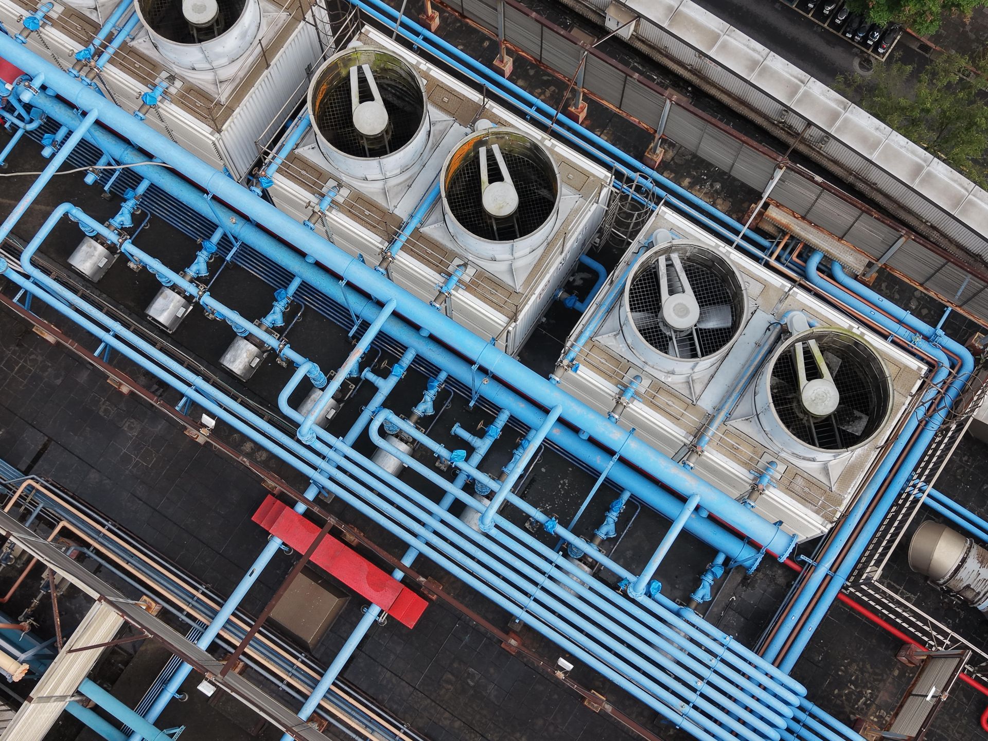 Aerial view of industrial cooling towers with blue pipes and a red structure alongside railroad tracks