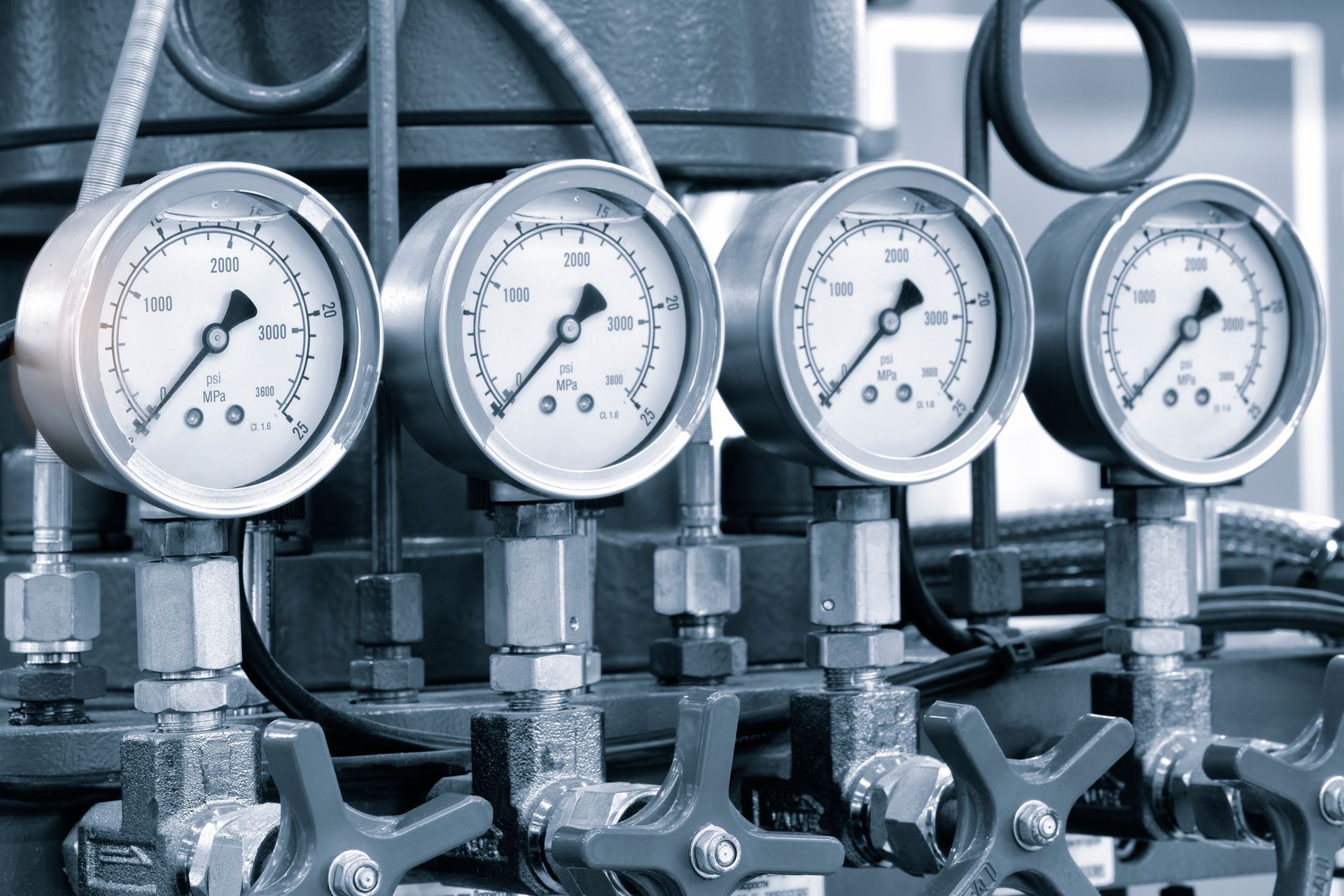 Four industrial pressure gauges and valves in a metal piping system