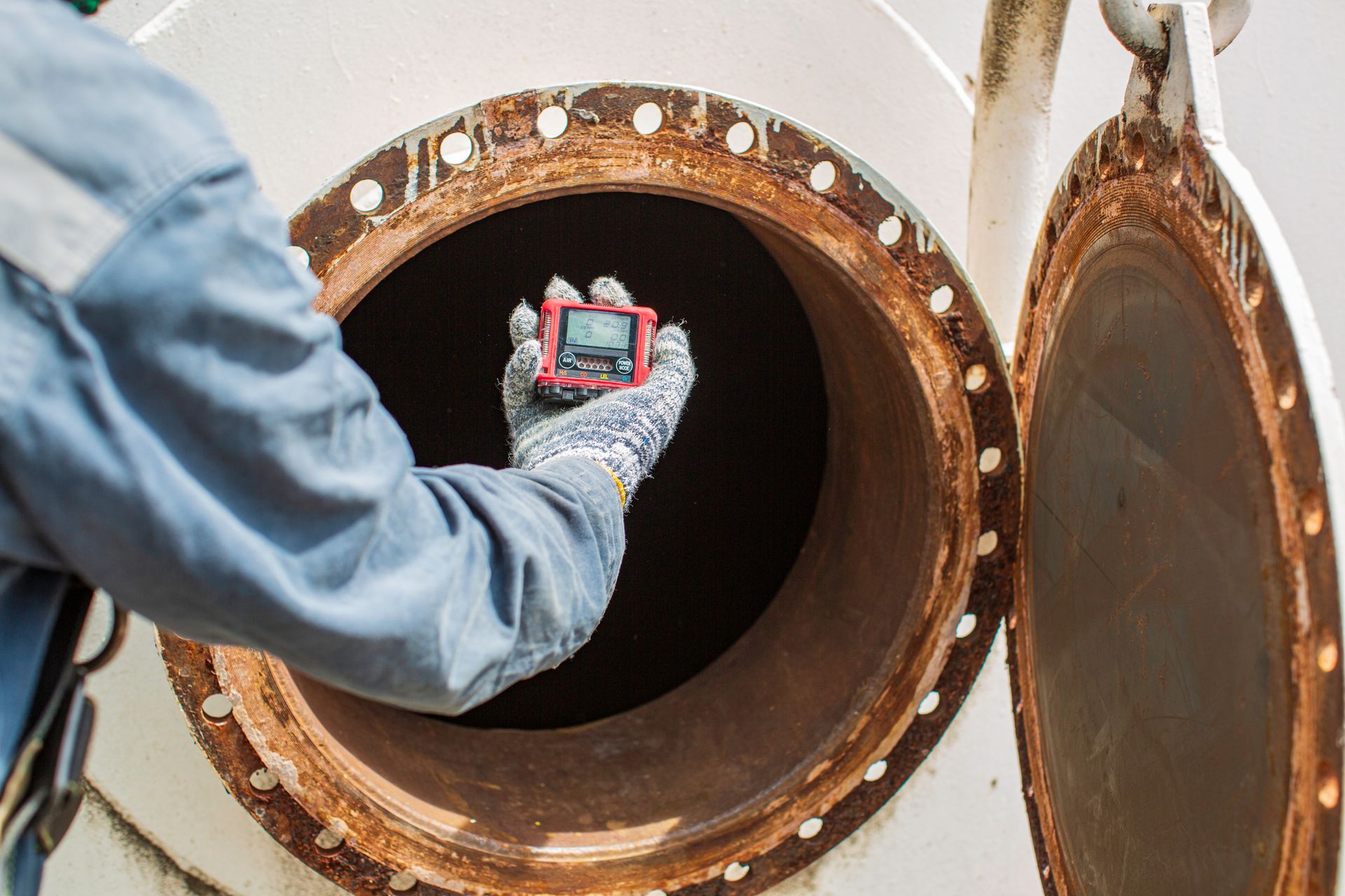 Gloved hand placing a device into a large rusty pipe opening during inspection