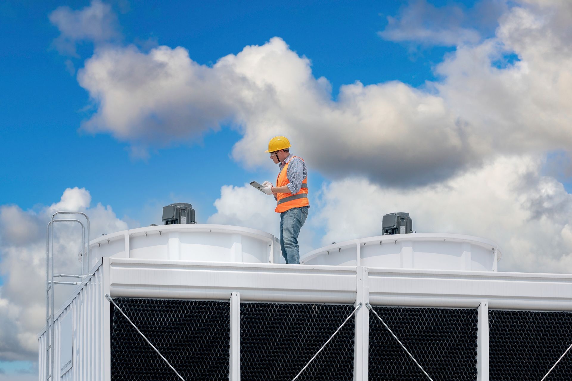 A man is standing on top of a cooling tower looking at a tablet.