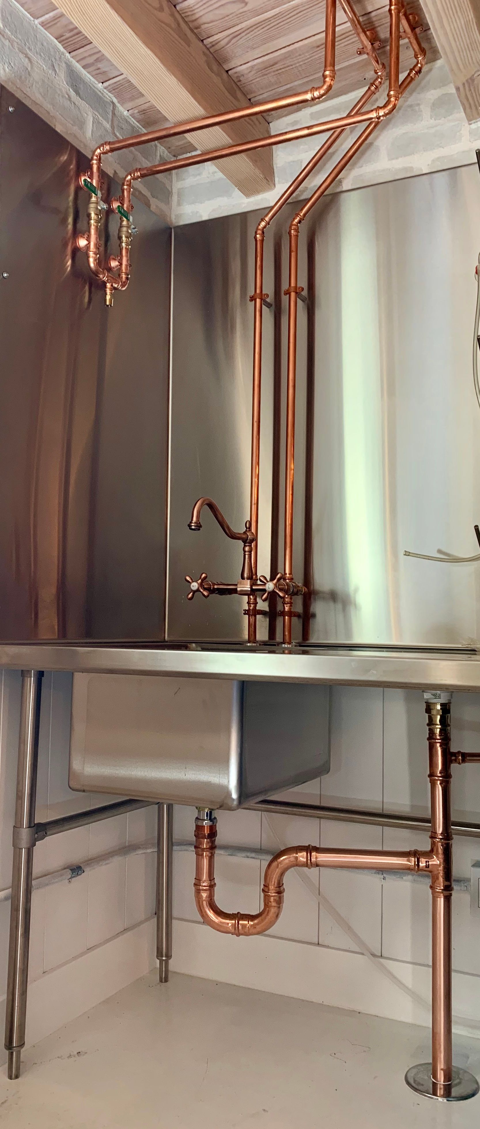 A kitchen sink with copper pipes coming out of it.