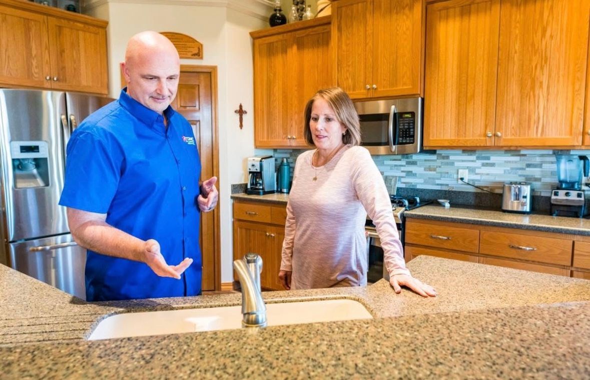 A man and a woman are standing in a kitchen looking at a sink.