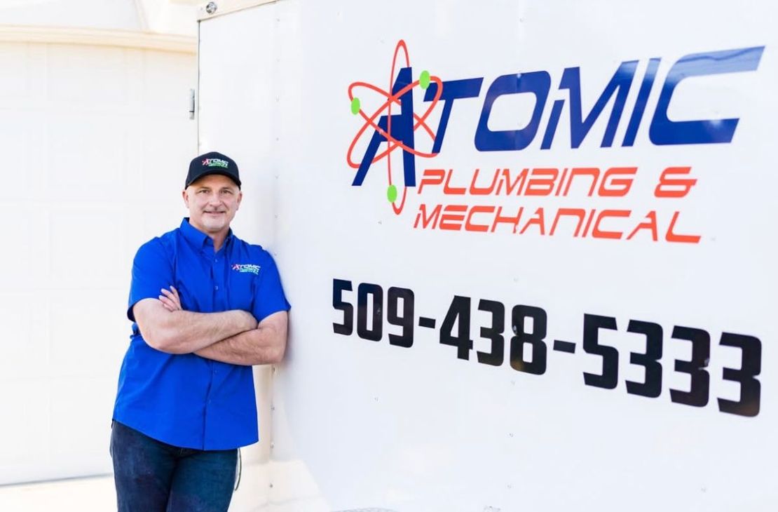 A man is standing in front of an atomic plumbing and mechanical truck.