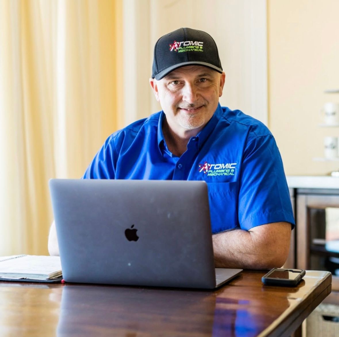 A man wearing an atomic hat sits in front of an apple laptop