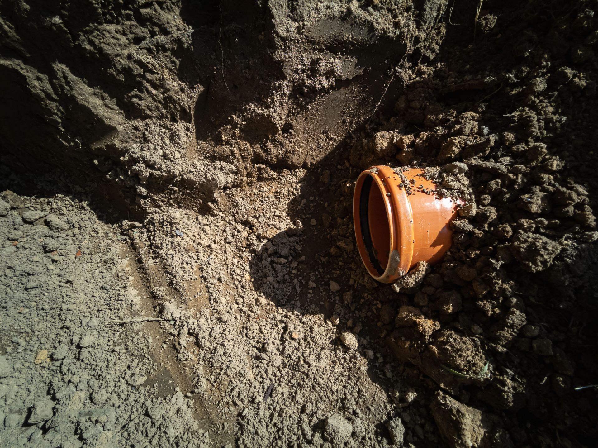 An orange pipe is laying in a pile of dirt