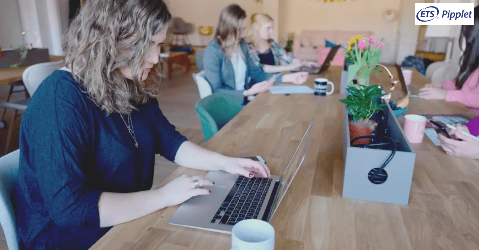 group of students sitting at a table concentrating on laptops