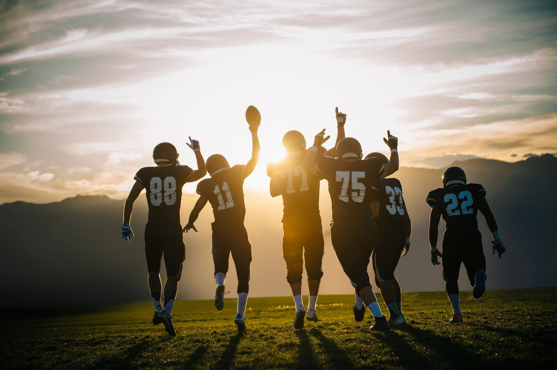 A group of football players are running on a field at sunset. A group of football players are running on a field at sunset.