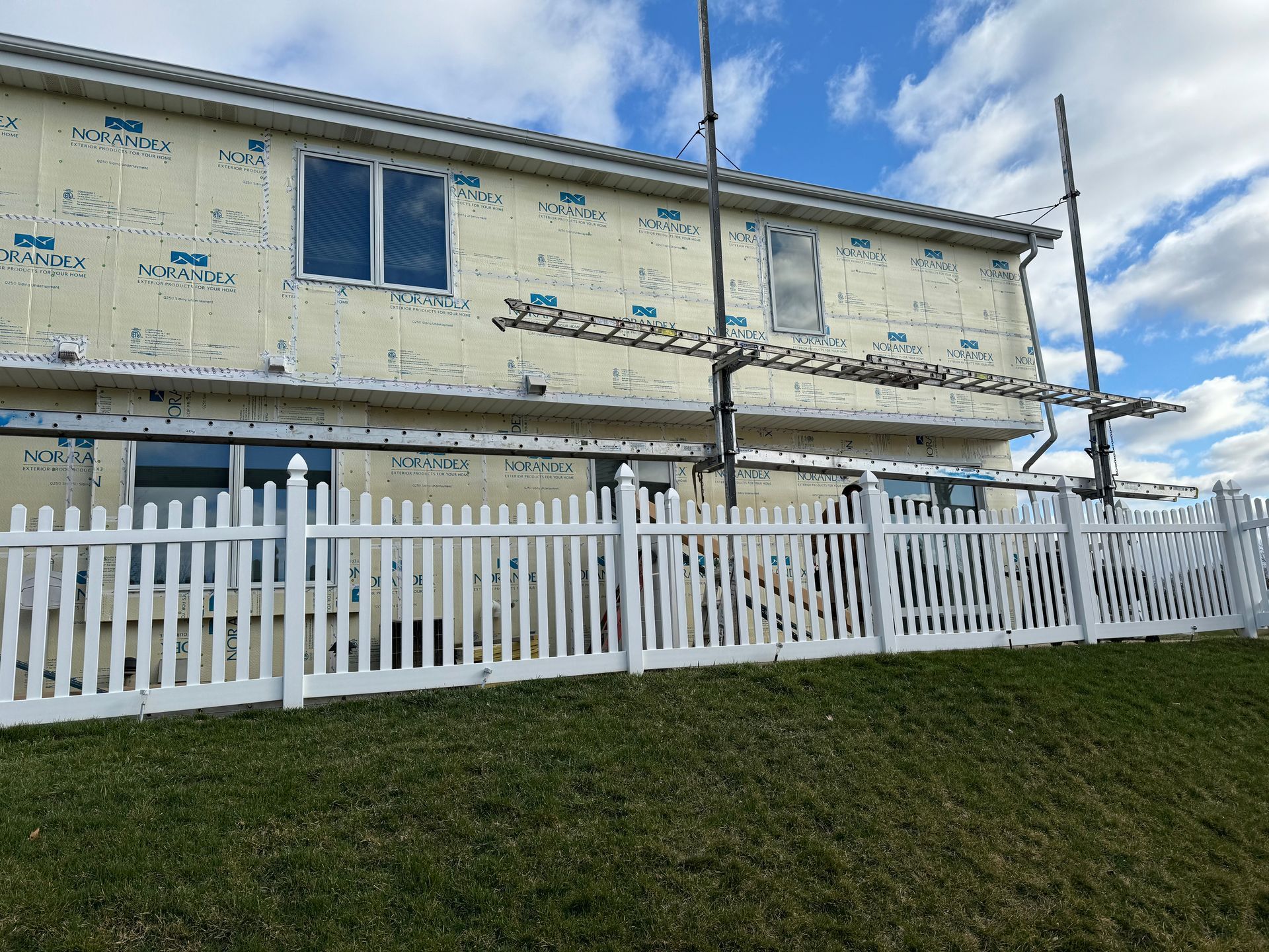 A white picket fence surrounds a house under construction.