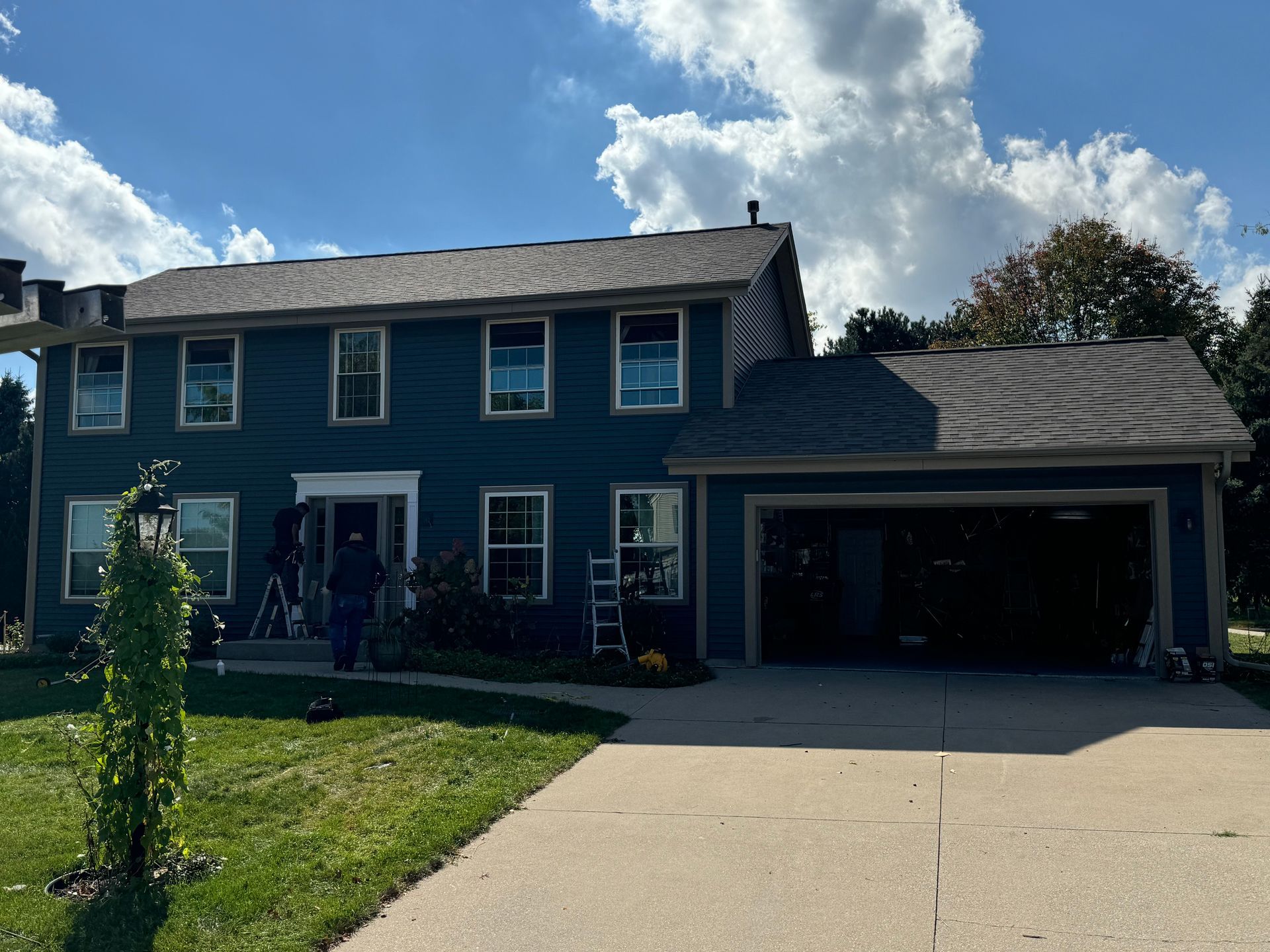 Two-story house in Janesville, WI with dark blue siding, brown roof, and open garage.