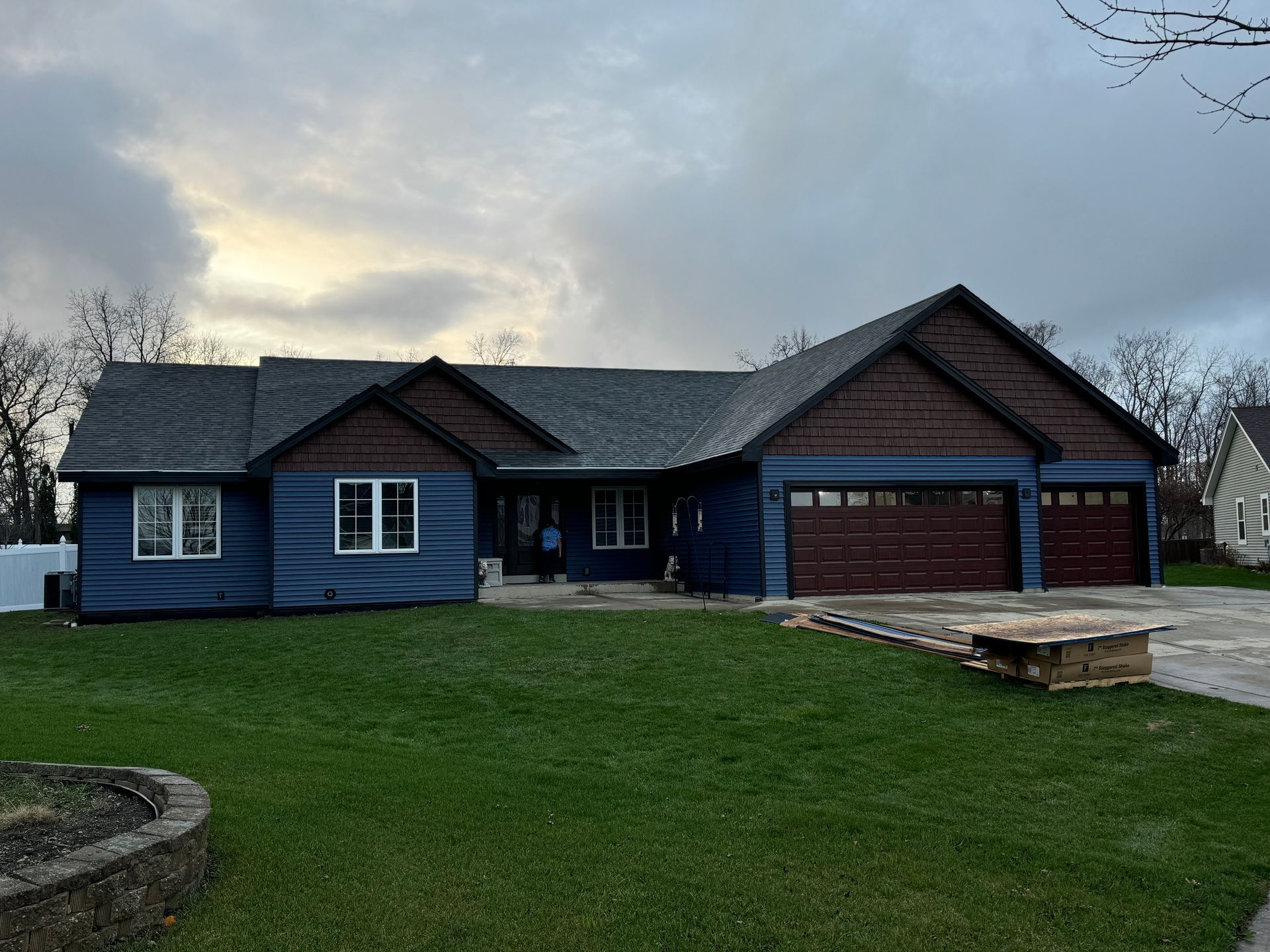 Blue house with brown trim and three-car garage on a green lawn under a cloudy sky.