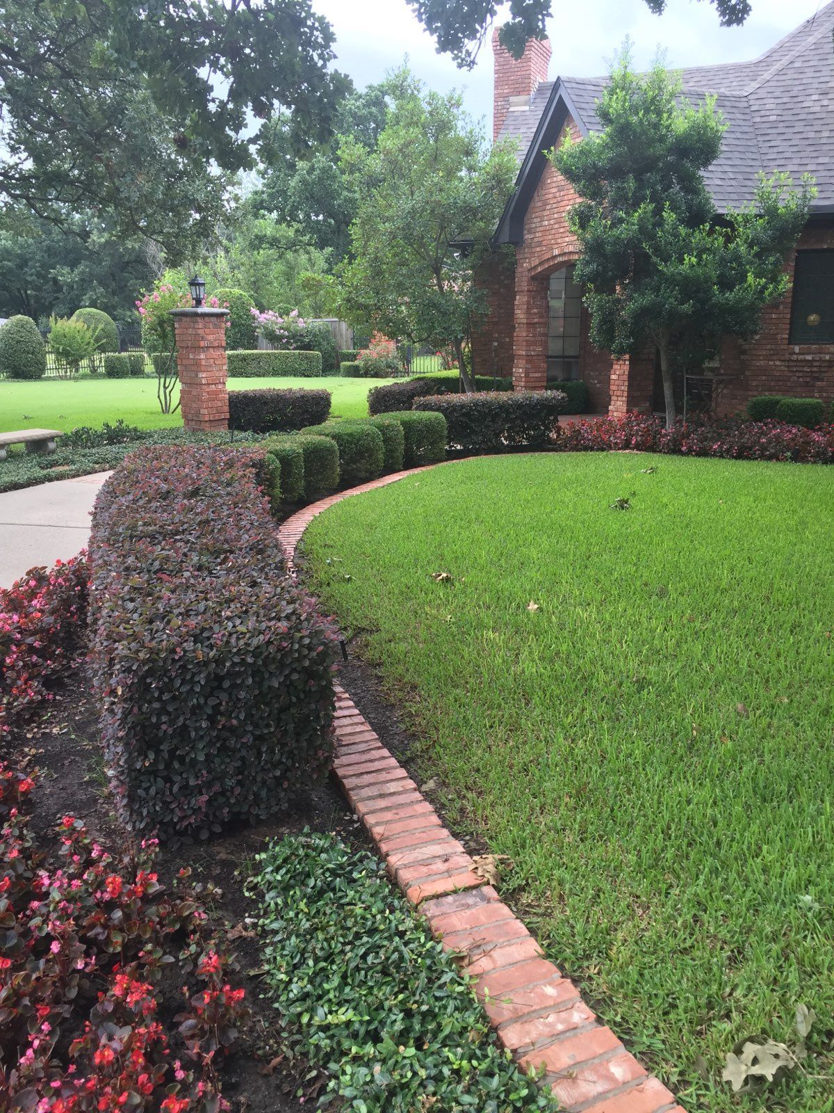 Brick house with manicured green lawn, hedges, and a flower bed in a landscaped front yard