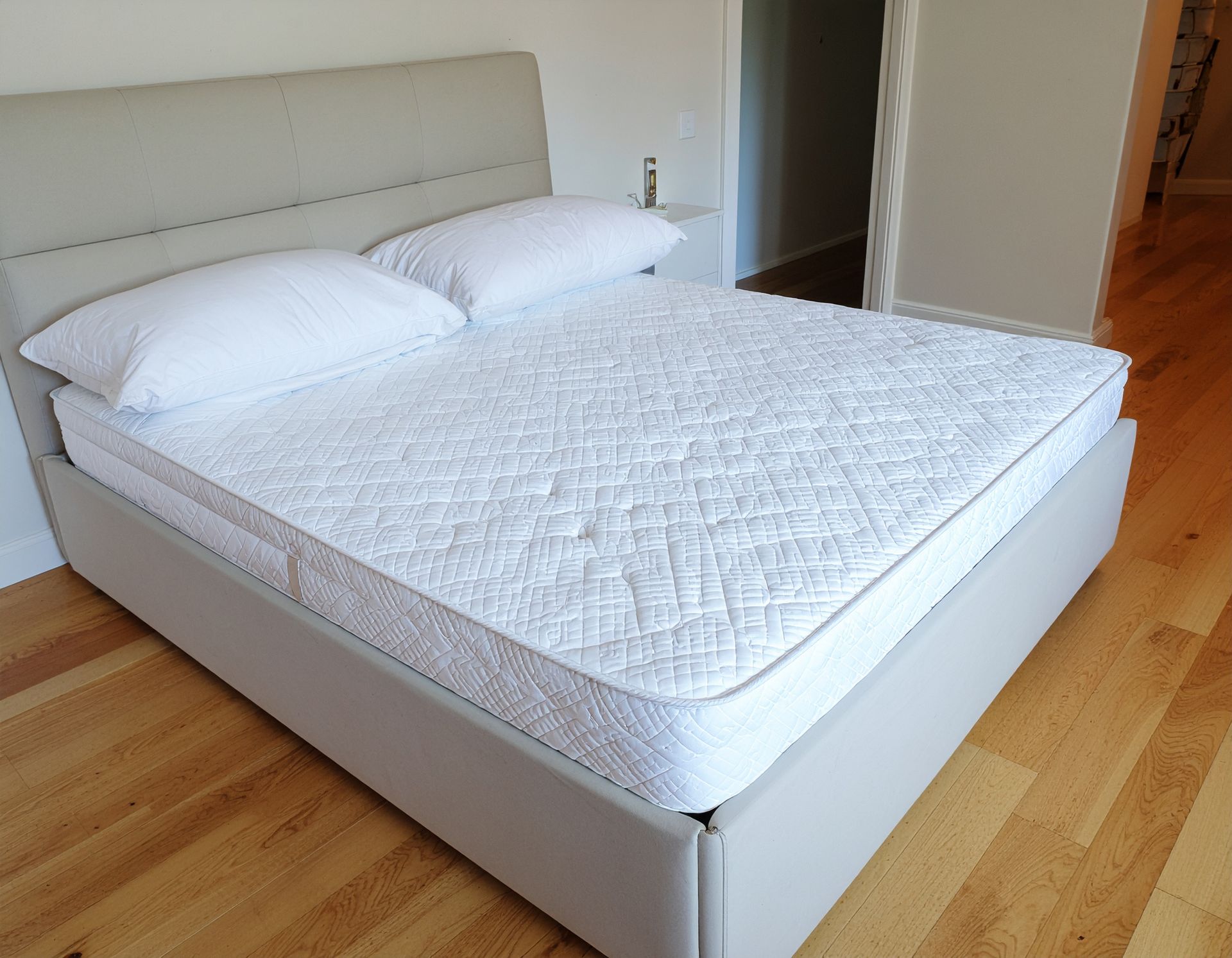 Bed with white mattress and pillows, gray headboard and frame. Wooden floor, room.