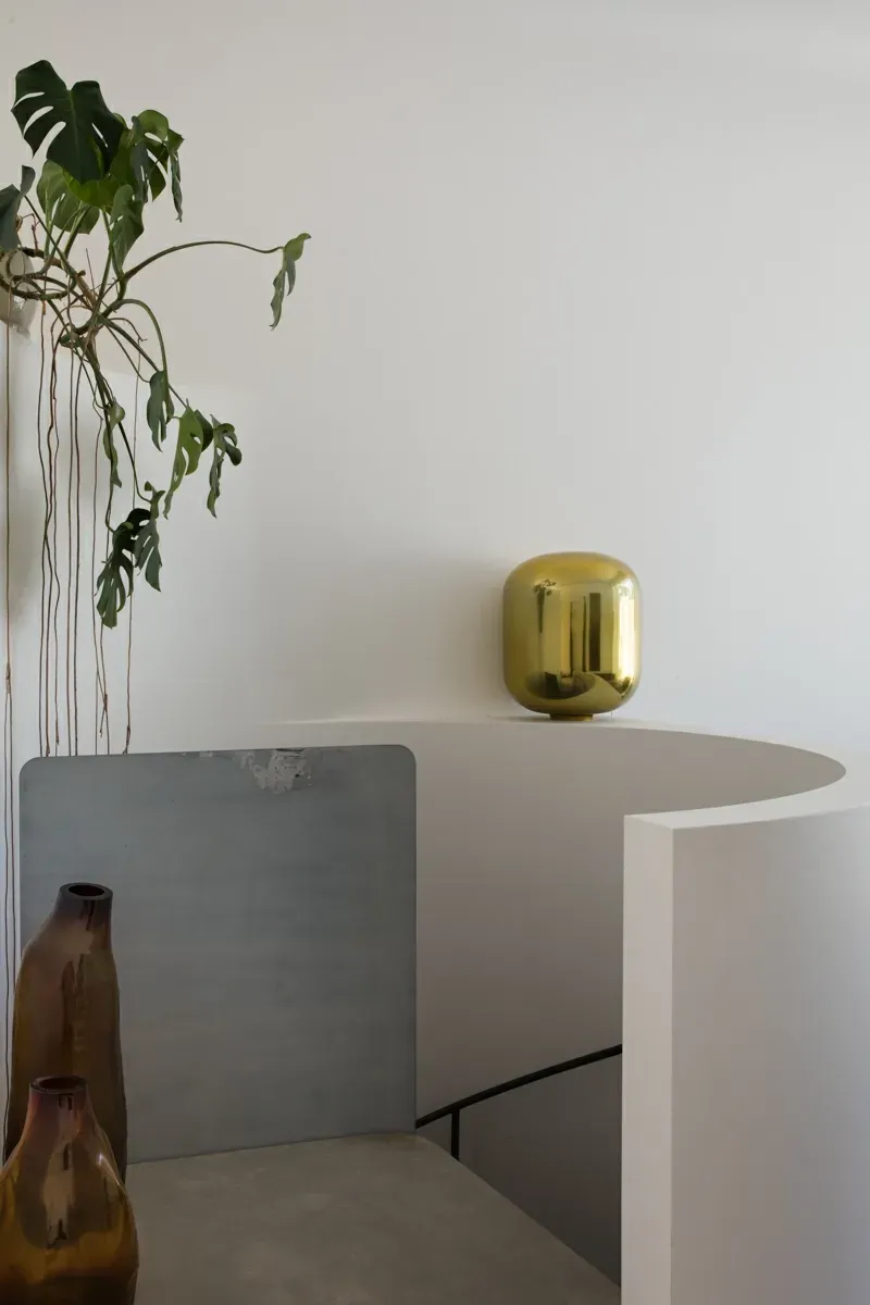 A gold vase is sitting on a staircase next to a plant.