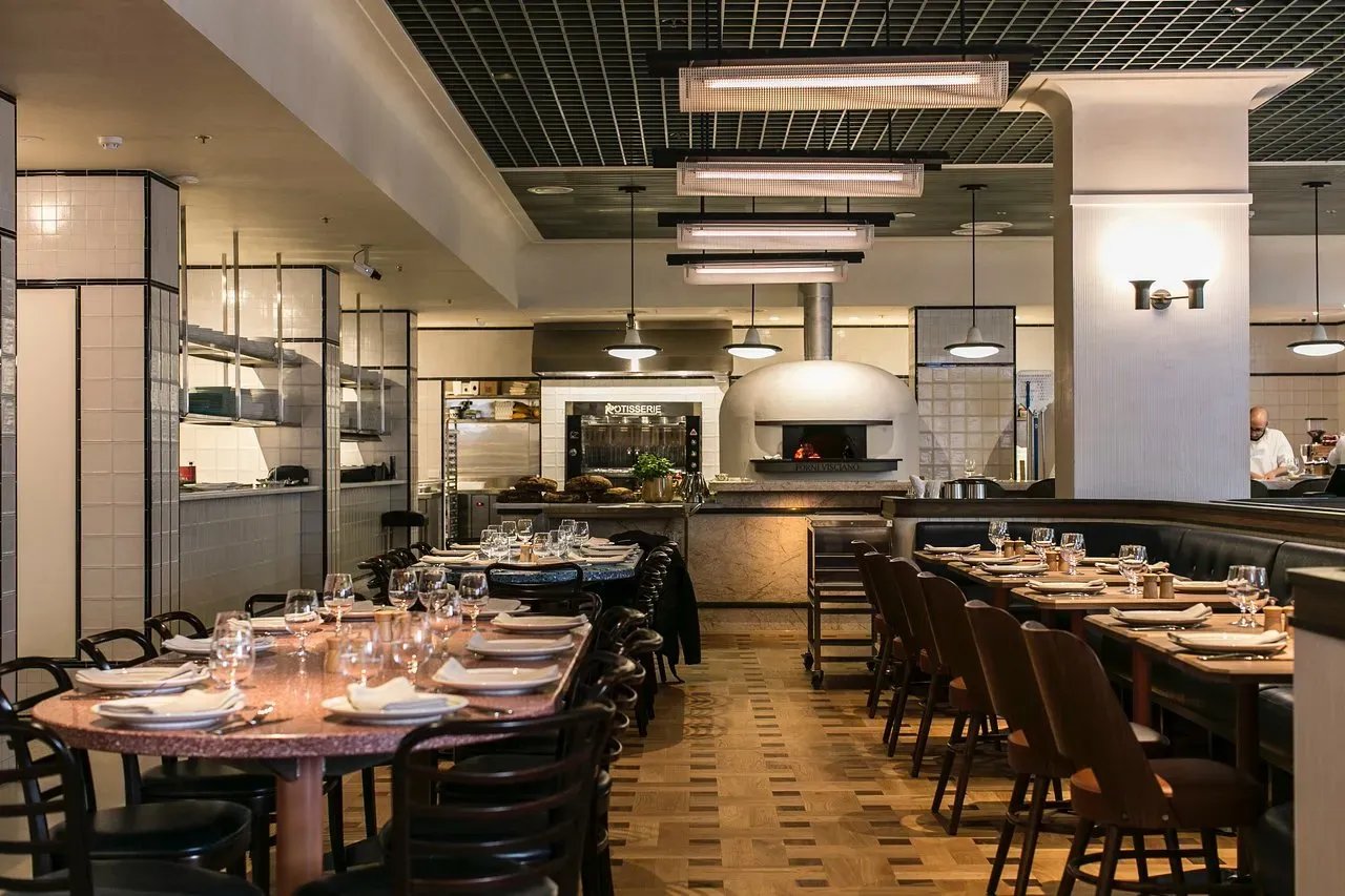 A restaurant with a lot of tables and chairs and a pizza oven.