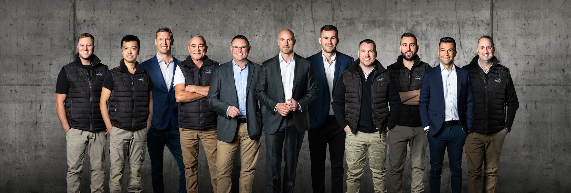 A group of men are standing next to each other in front of a concrete wall.