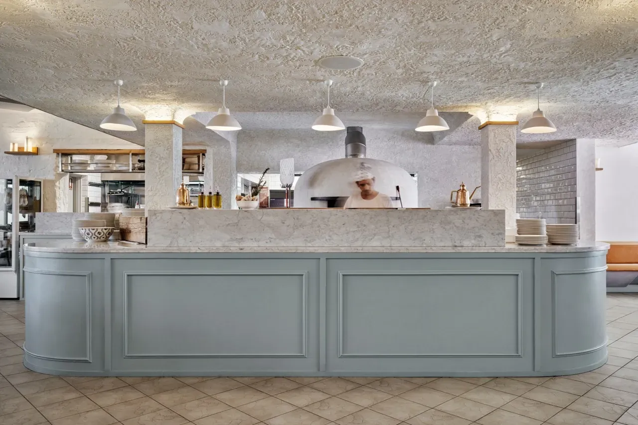 A large counter in a restaurant with a pizza oven in the background.