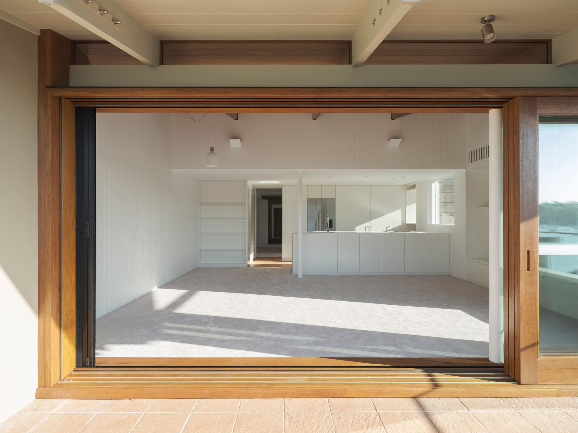 An empty room with a sliding glass door leading to a kitchen.