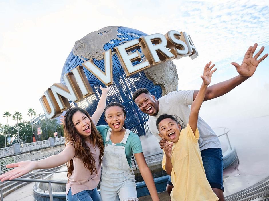 Four people posing in front of the Universal globe, smiling with arms raised at a theme park.