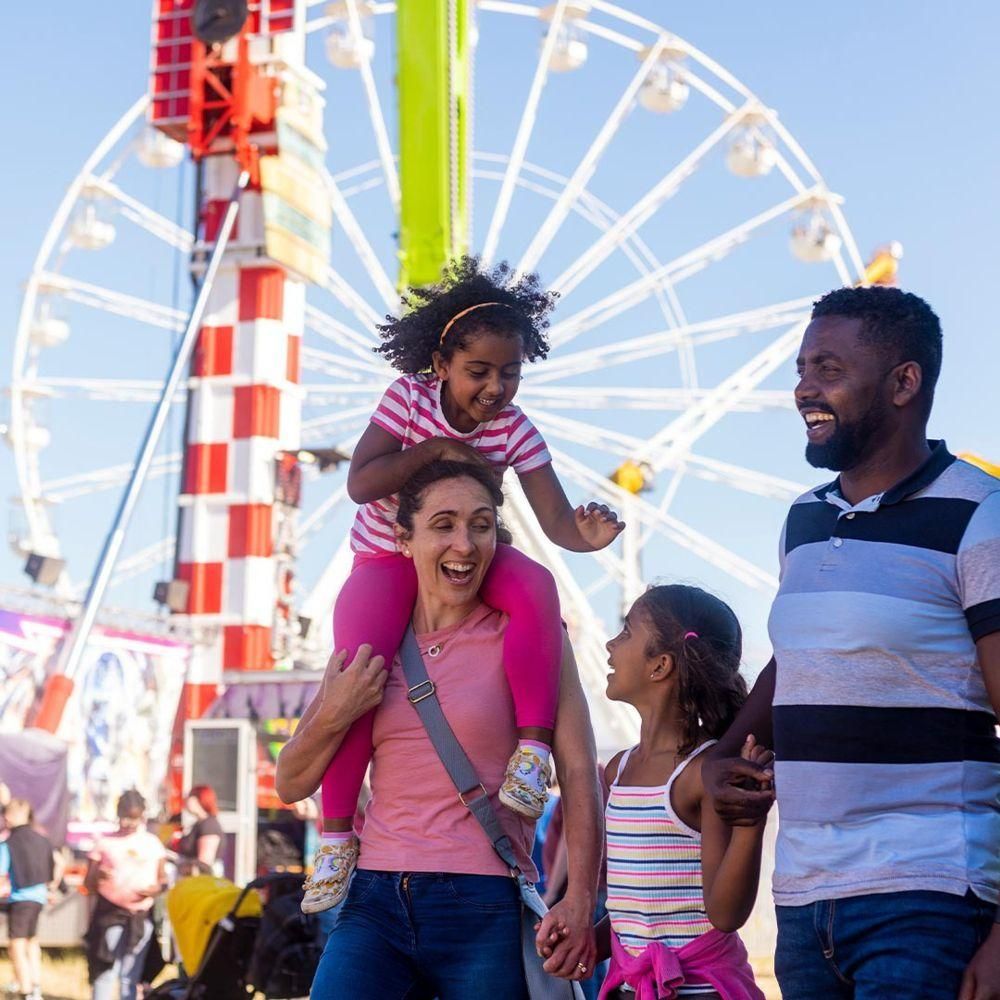 Explore Theme Park Vacations Family at an amusement park with a Ferris wheel in the background, smiling and playing together