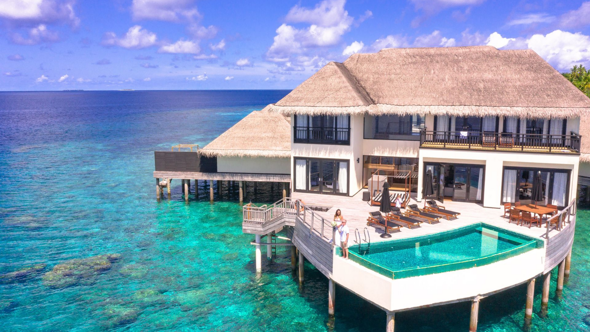 Oceanfront villa with a turquoise pool over clear blue water under a sunny sky