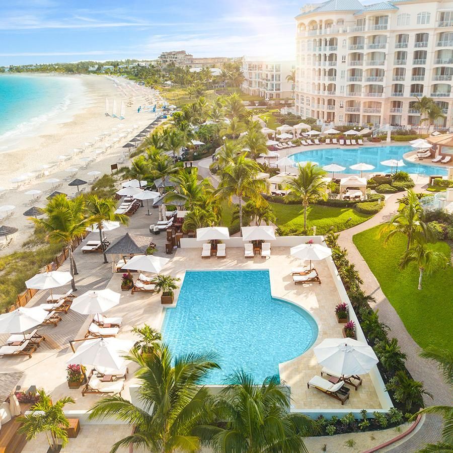 Explore All-Inclusive Vacations Oceanfront resort with turquoise pools, white umbrellas, palm trees, and a sandy beach at sunrise.