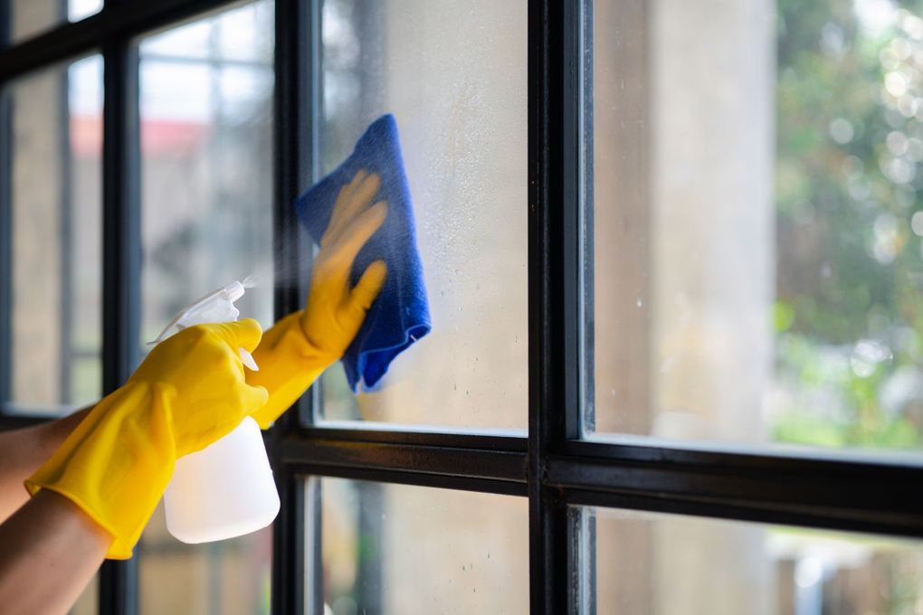 A person wearing yellow gloves is cleaning a window with a cloth.
