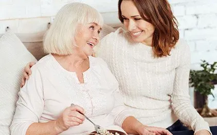 A young woman is feeding an older woman cereal on a bed.