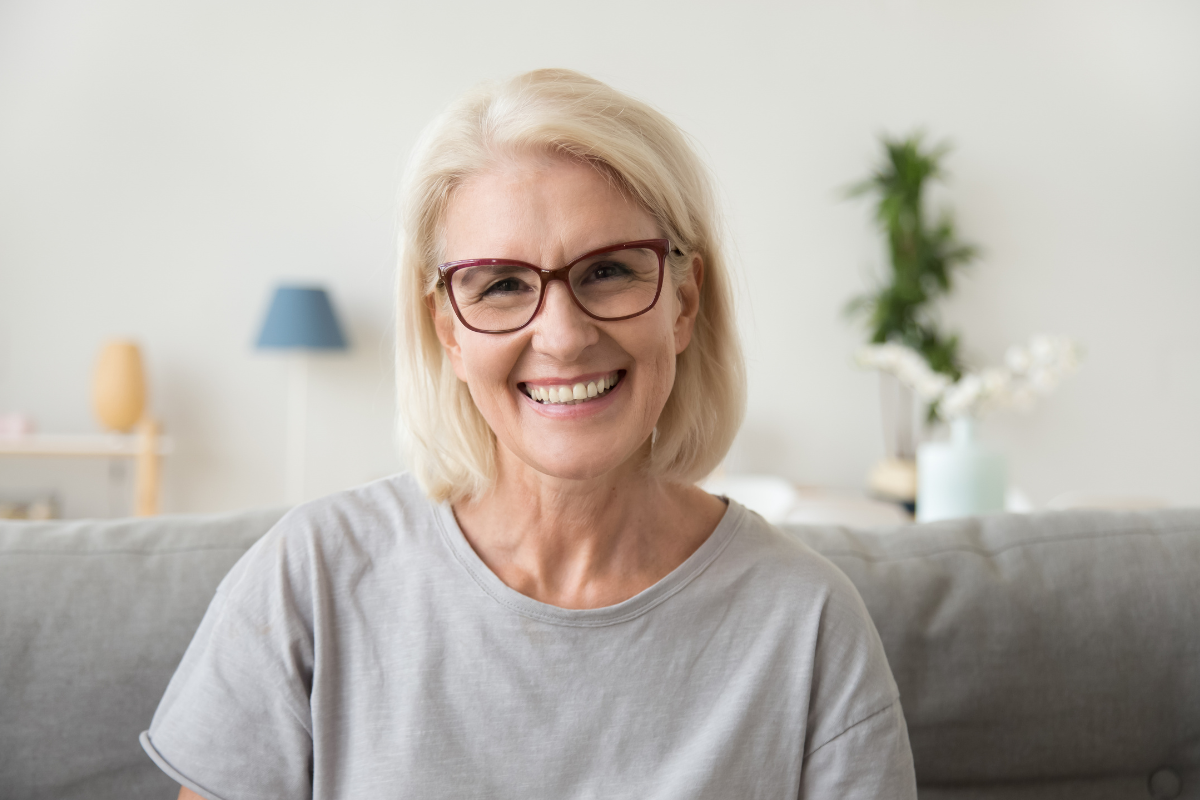 A woman wearing glasses is smiling while sitting on a couch.